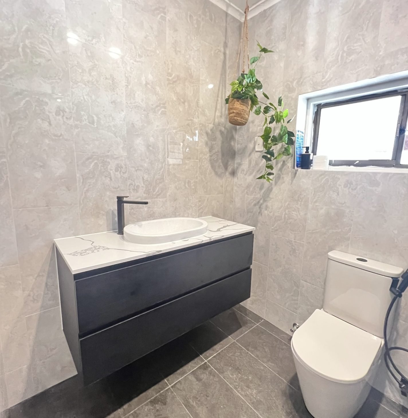 Renovated ensuite with a wall hung dark vanity, stone benchtop, vessel basin and black tapware