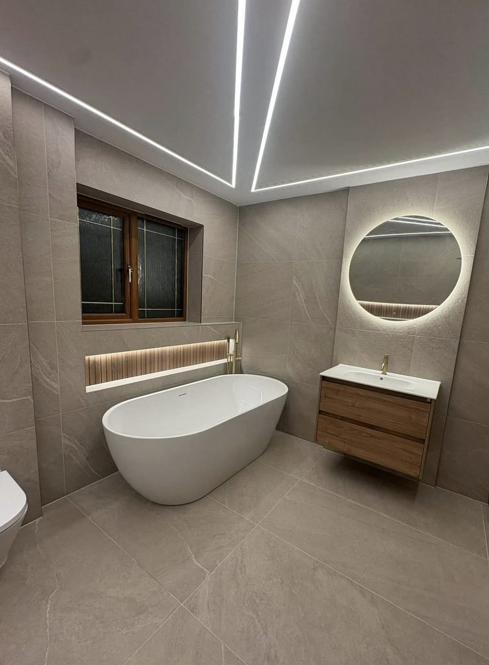 Freestanding bath in a stone effect tiled bathroom with LED ceiling strips