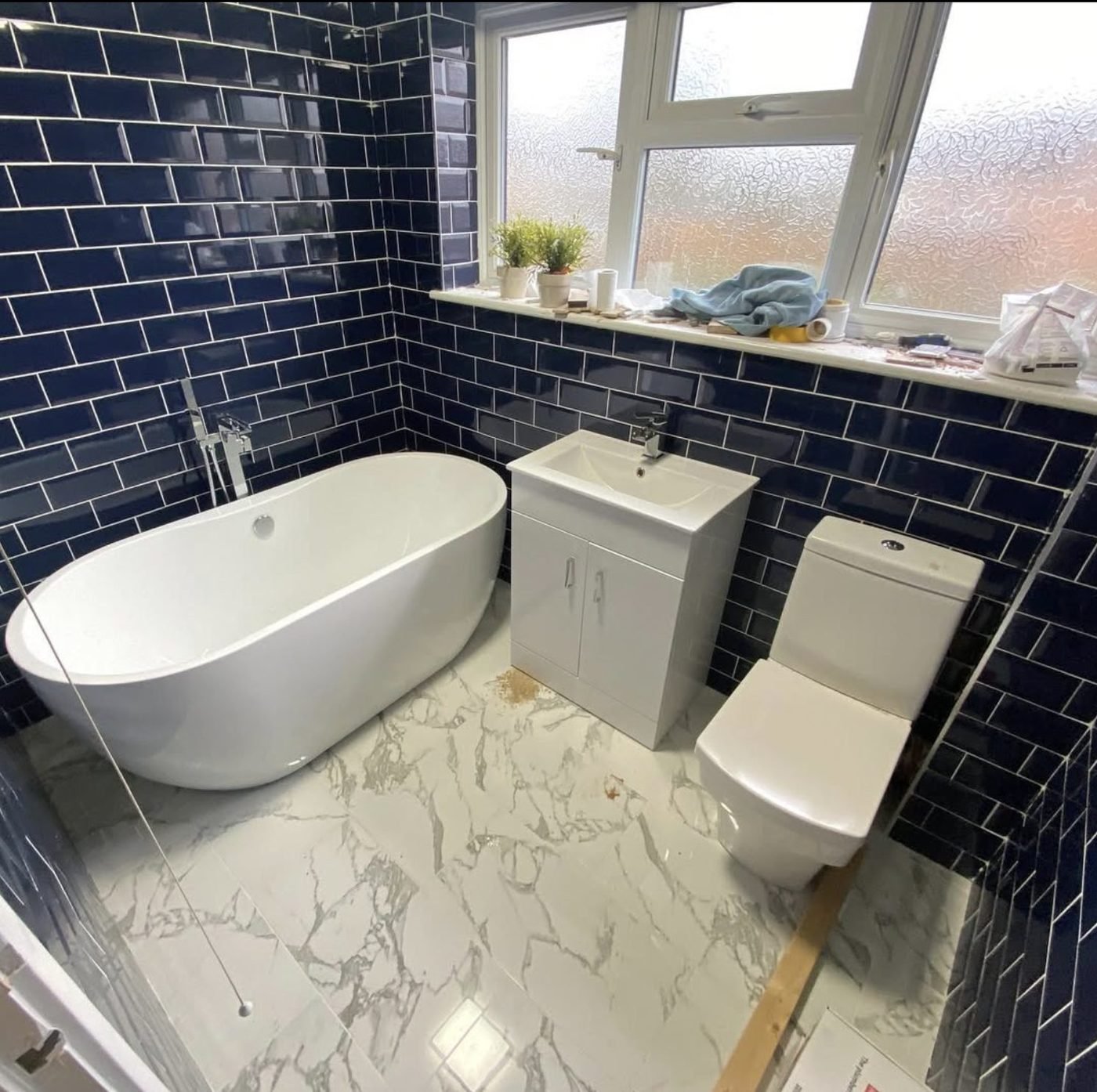 Navy subway tiled bathroom with a freestanding bath and marble effect floor