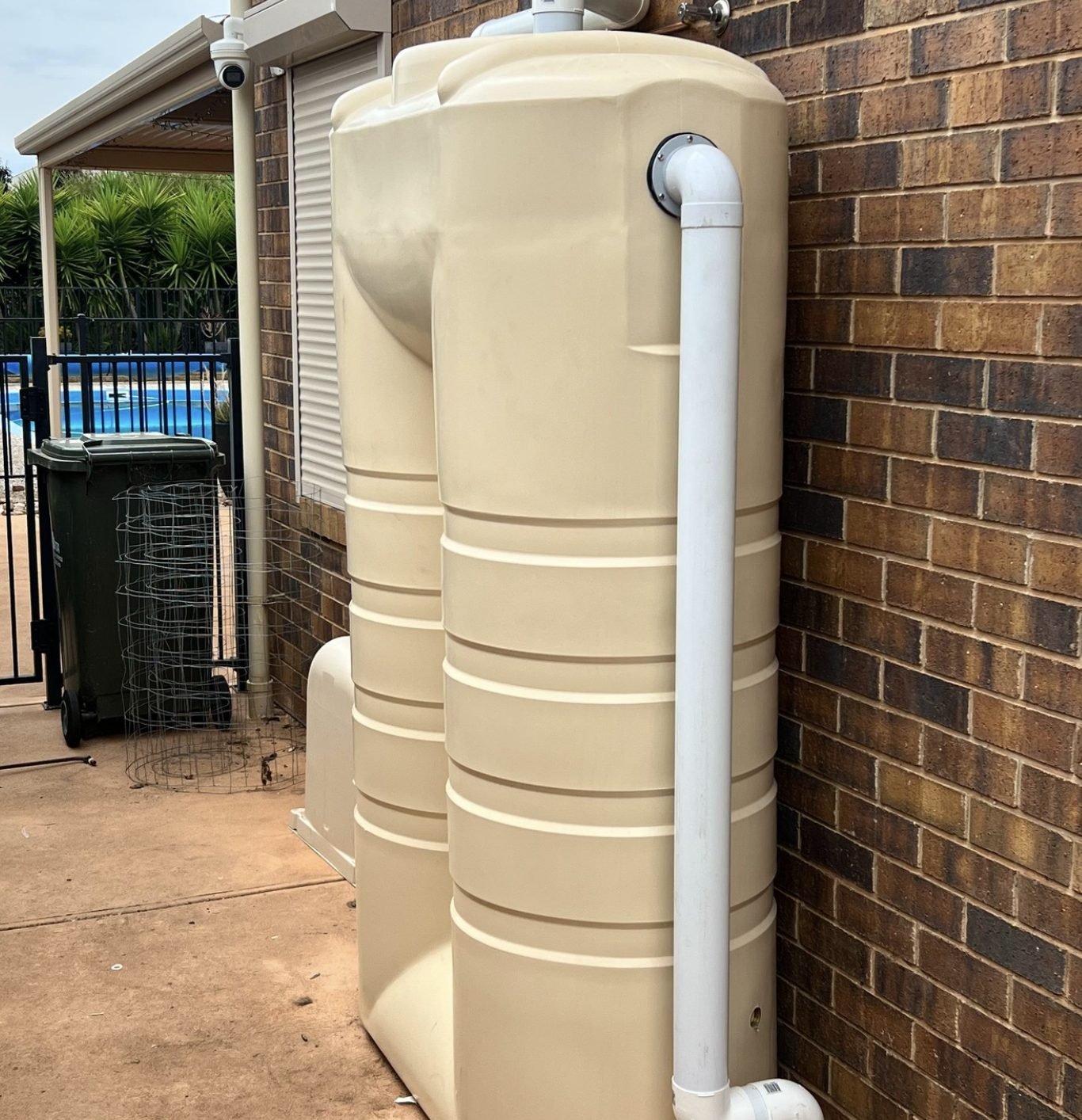 Two slimline rainwater tanks installed against a brick wall with downpipe and overflow plumbing
